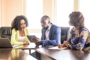 Young businessman with two young women in modern office. Man using digital tablet, female colleagues watching an listening, Nigeria, Africa.